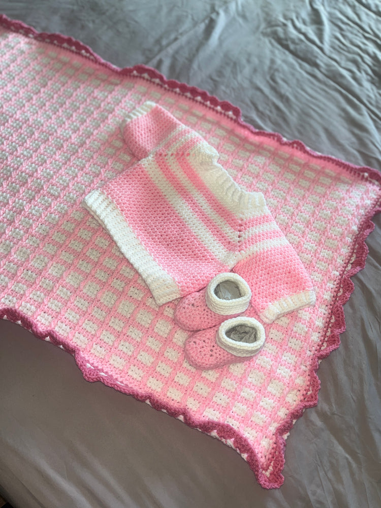 Pink-and-white crochet baby blanket with matching sweater and booties