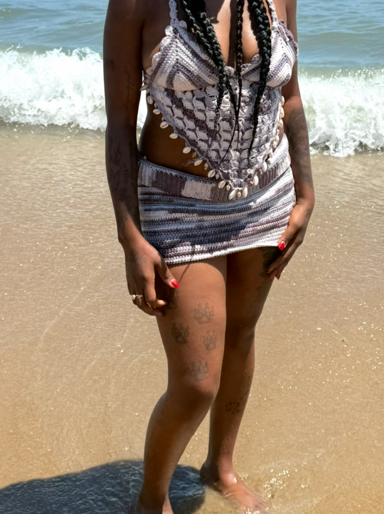 Woman smiling on the beach wearing a handmade crochet halter top and striped mini skirt set